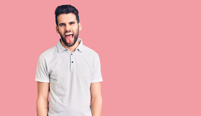 Fototapeta premium Young handsome man with beard wearing casual polo sticking tongue out happy with funny expression. emotion concept.
