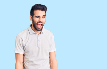 Young handsome man with beard wearing casual polo winking looking at the camera with sexy expression, cheerful and happy face.