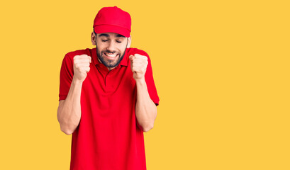 Fototapeta premium Young handsome man with beard wearing delivery uniform excited for success with arms raised and eyes closed celebrating victory smiling. winner concept.