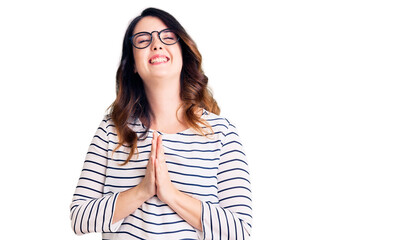 Beautiful young brunette woman wearing casual clothes and glasses begging and praying with hands together with hope expression on face very emotional and worried. begging.