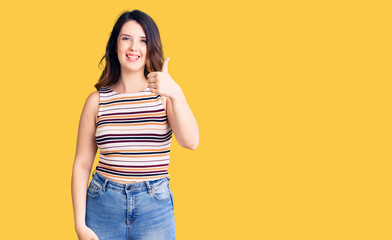 Beautiful young brunette woman wearing casual clothes smiling happy and positive, thumb up doing excellent and approval sign