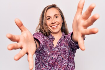 Young beautiful blonde woman wearing boho shirt standing over isolated background looking at the camera smiling with open arms for hug. cheerful expression embracing happiness.