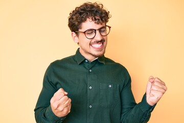 Young caucasian man with curly hair wearing casual clothes and glasses excited for success with...
