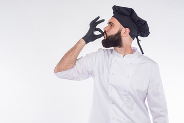 The chef approves. The bearded chef makes a sign with his hands very tasty. Excellent cuisine. A chef in a black hat and gloves. Man on a white background with a space for text.