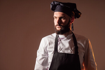 Portrait of the chef. A man in a chef's uniform looks into the distance. A bearded cook on a brown background. Professions.