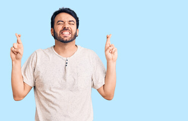 Fototapeta premium Young hispanic man wearing casual clothes gesturing finger crossed smiling with hope and eyes closed. luck and superstitious concept.