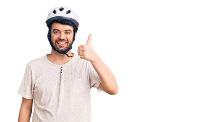 Young hispanic man wearing bike helmet smiling happy and positive, thumb up doing excellent and approval sign