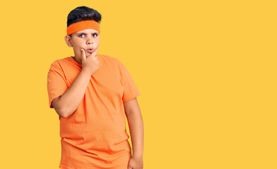 Little boy kid wearing sportswear looking fascinated with disbelief, surprise and amazed expression with hands on chin