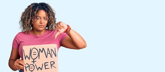 Young african american plus size woman holding woman power banner with angry face, negative sign showing dislike with thumbs down, rejection concept