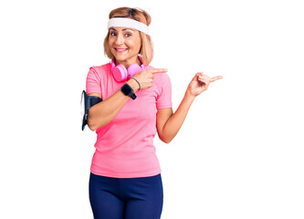 Obraz na płótnie Canvas Young blonde woman wearing sportswear and headphones smiling and looking at the camera pointing with two hands and fingers to the side.
