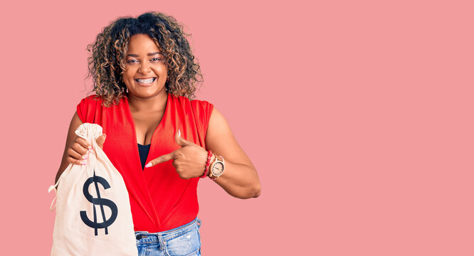 Young african american plus size woman holding money bag with dollar symbol smiling happy pointing with hand and finger