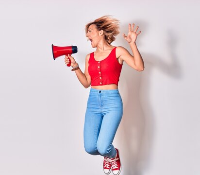 Young beautiful caucasian woman screaming using megaphone. Jumping over isolated white background
