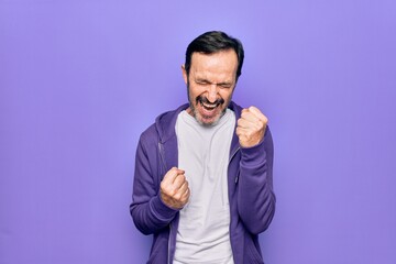 Middle age handsome sporty man wearing casual purple sweatshirt over isolated background celebrating surprised and amazed for success with arms raised and eyes closed