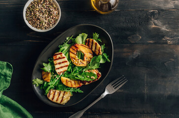 Grilled Halloumi Cheese salad with peach and arugula on a black wooden background. Healthy food concept.