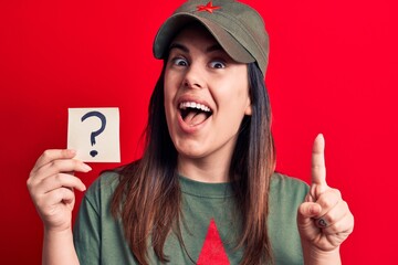 Beautiful woman wearing cap with red star communist symbol holding question mark reminder smiling with an idea or question pointing finger with happy face, number one