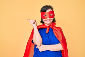 Brunette woman with down syndrome wearing super hero costume smiling happy pointing with hand and...