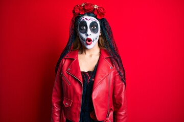 Woman wearing day of the dead costume over red afraid and shocked with surprise expression, fear and excited face.