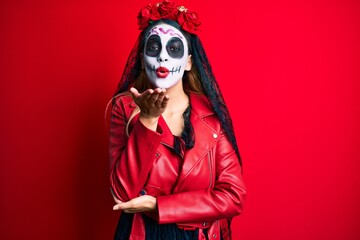 Woman wearing day of the dead costume over red looking at the camera blowing a kiss with hand on air being lovely and sexy. love expression.