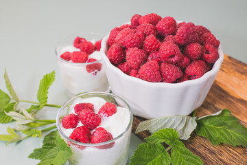 Lots of raspberries in plate on wooden tray. Desserts are on table decorated with delicious ripe berries.