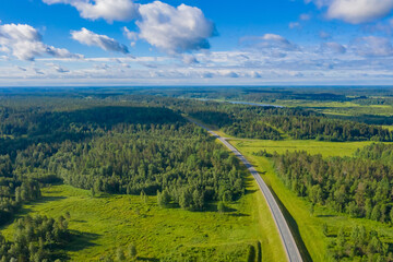 Fototapeta na wymiar Highway and forests aerial photography. The road passes through the forest. Highway and beautiful natural landscape around. The forest and the road under the blue sky. Travel by car.