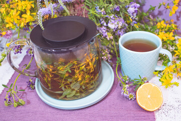 Medicinal tea from the herb hypericum. A glass teapot with yellow flowers and a mug with a drink. Eco food.