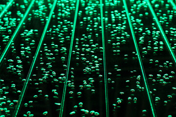 Bright green lines and air bubbles behind a glass wall of water. Black background.