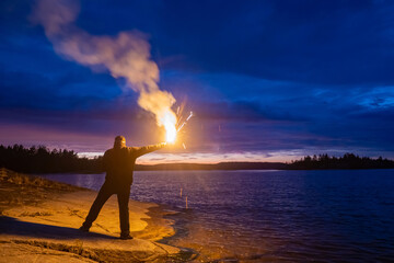 Smoke signal. A man with a smoke torch in the evening by the water. Rescue. SOS. Distress signal....