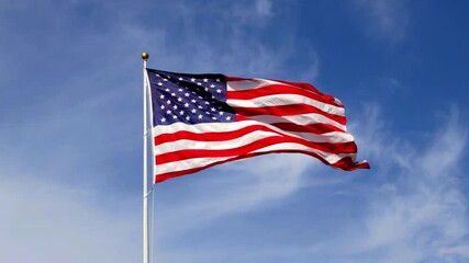 American flag waving in slow motion, with vibrant red white and blue colors lit by the sun, against blue sky for with copy space.