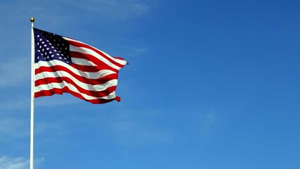 American flag waving in the wind in slow motion, with vibrant red white and blue colors against blue sky, with copy space. - Powered by Adobe