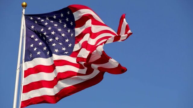 Bright American flag waving in the wind, in slow motion, with vibrant red white and blue colors lit by the sun, against blue sky for with copy space.
