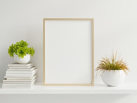 Wooden frame leaning on white shelf in bright interior with plants on the table with plants in pots on empty wall background.