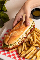 Mano de hombre comiendo sanduche de chorizo comida tradicional argentina llamada choripan con papas fritas