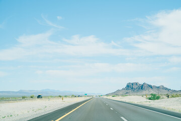 landscape of straight road running along barren land on both side. view of freeway stretches all the way to horizon on a sunny day.