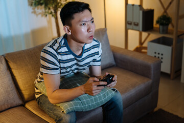 concentrated young asian korean guy enjoying video game in dark house living room at late night....