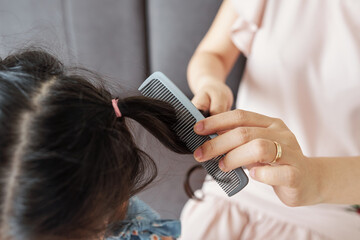 Naklejka premium Close-up image of mother combing hair of her little daughter