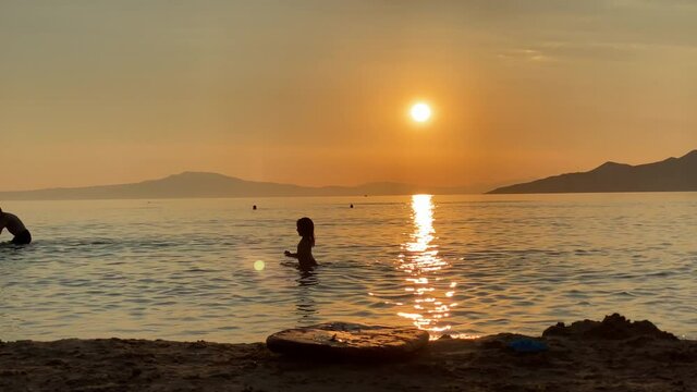 Silhouette of a young girl playing in the sea on sunset