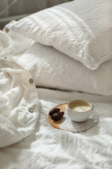Cup of fresh coffee in bed on ceramic tray, morning mood. Linen cotton textile bedclothes. Organic and natural linen. Cozy bedroom interior. Beautiful light.