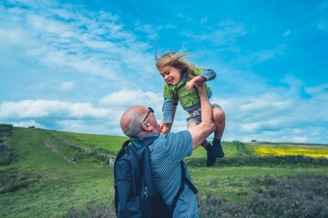 Grandfather liftingh his preschooler grandchild in a meadow - obrazy, fototapety, plakaty