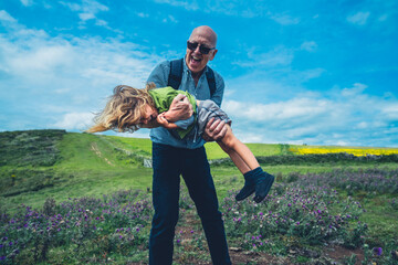 Grandfather liftingh his preschooler grandchild in a meadow