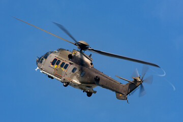 Camouflaged military helicopter flying at a steep angle.