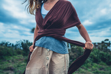 Young woman in meadow tying baby carrier sling
