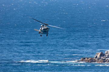 Navy helicopter flying at low altitude over the ocean near a coastline.