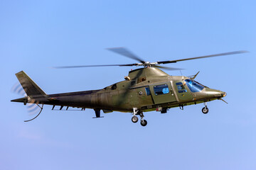 Green army helicopter flying against a clear blue sky.