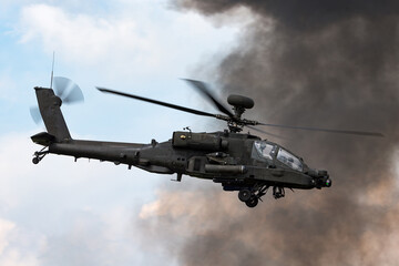 Army attack helicopter flying past dark smoke plumes.