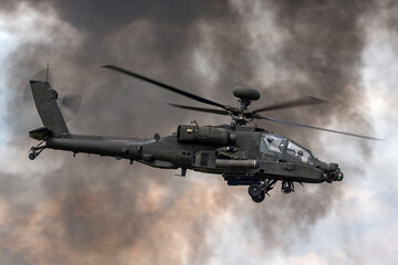 Fototapeta na wymiar Army attack helicopter flying past dark smoke plumes.