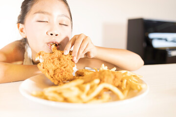 A cute Asian girl is enjoying eating fried chicken and French fries.