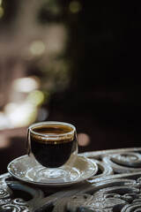 One hot black coffee on outdoor table in a transparent glass with blurry bokez background