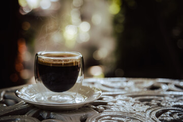 One hot black coffee on outdoor table in a transparent glass with blurry bokez background