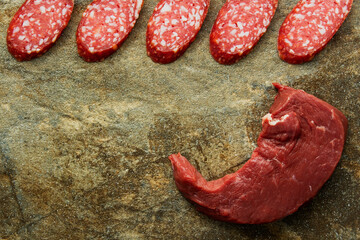 Fresh raw beef steak, meat and slices of sliced sausage on a background of granite stone, close-up.