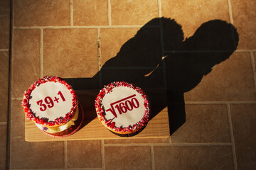 A cake with white icing, two cakes with mathematical formulas on a wooden stand.